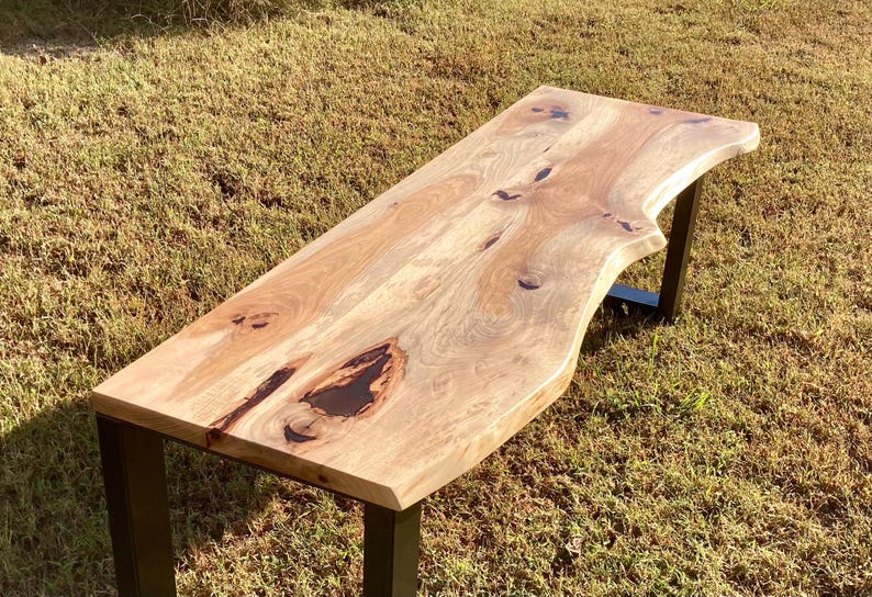May include: A long, wooden table with a live edge top and black metal legs. The table top has a natural wood grain and a dark brown stain.