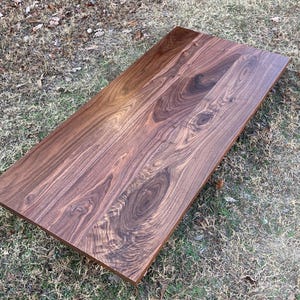 May include: A large, rectangular slab of dark brown walnut wood with a natural, polished finish. The wood grain is visible and has a rich, intricate pattern.