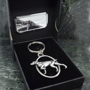 May include: A silver key chain with a detailed dog figurine in an oval frame. The keychain is in a black gift box with a silver plaque that reads "Your Personal Message Engraved".