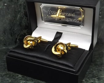 Puede incluir: Gemelos de nudo dorados en una caja de regalo negra con una placa plateada que dice "Su mensaje personal grabado".