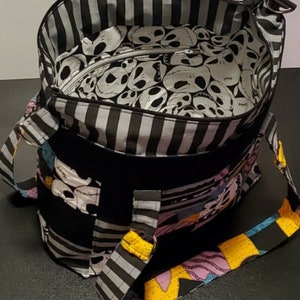 May include: Black and white striped tote bag with a Nightmare Before Christmas fabric design. The bag has a black and white striped lining and a zipper closure. The bag has a black and white striped strap and a yellow, pink, and blue strap.