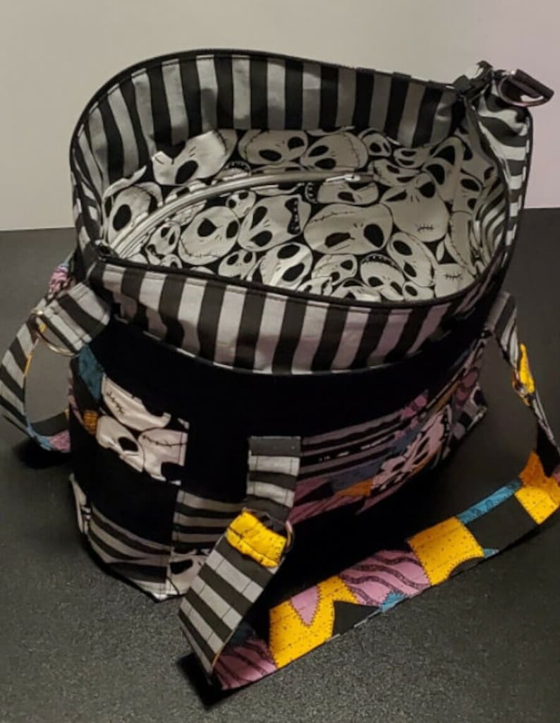 May include: Black and white striped tote bag with a Nightmare Before Christmas fabric design. The bag has a black and white striped lining and a zipper closure. The bag has a black and white striped strap and a yellow, pink, and blue strap.