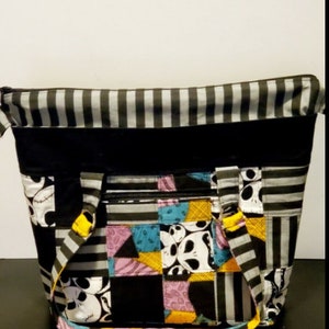 May include: A black and white striped tote bag with a patchwork design featuring characters from the Nightmare Before Christmas. The bag has a zipper closure and two yellow straps.