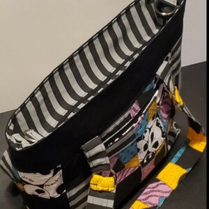 May include: Black and white striped tote bag with a patchwork design featuring characters from The Nightmare Before Christmas. The bag has two black handles and a zipper closure.