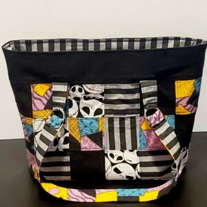 May include: A black patchwork tote bag with a striped lining. The bag features a patchwork design of black, white, gray, yellow, pink, and blue fabric with a repeated pattern of Jack Skellington's face from the Nightmare Before Christmas.