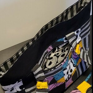 May include: Black and white striped tote bag with a patchwork design featuring characters from The Nightmare Before Christmas. The bag has a black lining and a yellow and black striped strap.