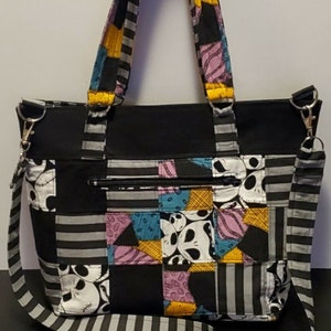 May include: A black and white striped tote bag with a patchwork design featuring Jack Skellington's face. The bag has a zippered pocket and a detachable shoulder strap.