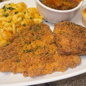 Op de afbeelding: Een bord met eten met twee stukken gebakken kip, macaroni en kaas en een bijgerecht van zoete aardappelen. De kip is goudbruin en knapperig, en de macaroni en kaas zijn romig en kaasachtig.