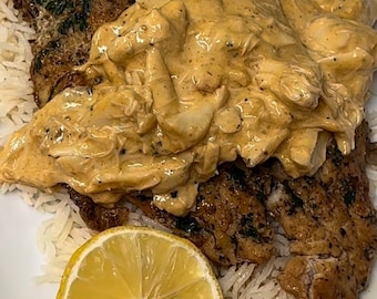 以下が含まれることがあります： 魚が2切れ、クリーミーなソース、レモンのくさび形が乗った料理のプレート。魚はクリーミーなソースで覆われており、プレートは白いご飯で囲まれています。