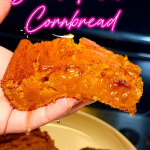 Puede incluir: Un primer plano de un pan de maíz de batata, una rebanada se sostiene para mostrar el interior. El pan de maíz es de color marrón dorado y tiene una textura húmeda y desmenuzable. El texto "Sweet Potato Cornbread" está escrito en letras de neón rosa en la parte superior de la imagen.