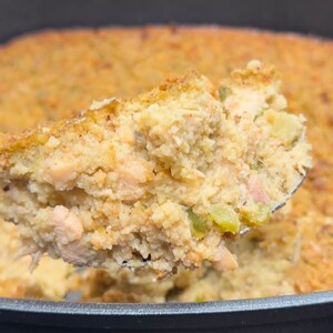 Puede incluir: Un primer plano de una cuchara sacando una porción de una fuente de horno llena de un relleno dorado y sabroso. El relleno está hecho con pan rallado, verduras y carne.