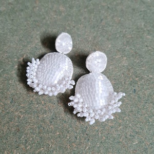 May include: A pair of white beaded earrings with a teardrop shape and a fringe of beads hanging from the bottom.