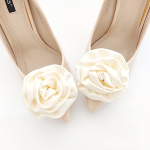 Op de afbeelding: Een paar nudekleurige hoge hakken met ivoorwitte satijnen rozen op de tenen.