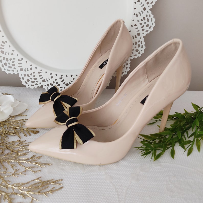 May include: A pair of nude high-heeled pumps with black and gold bows on the toes.