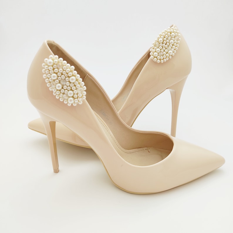 May include: A pair of nude-colored high-heeled shoes with pearl embellishments on the straps.