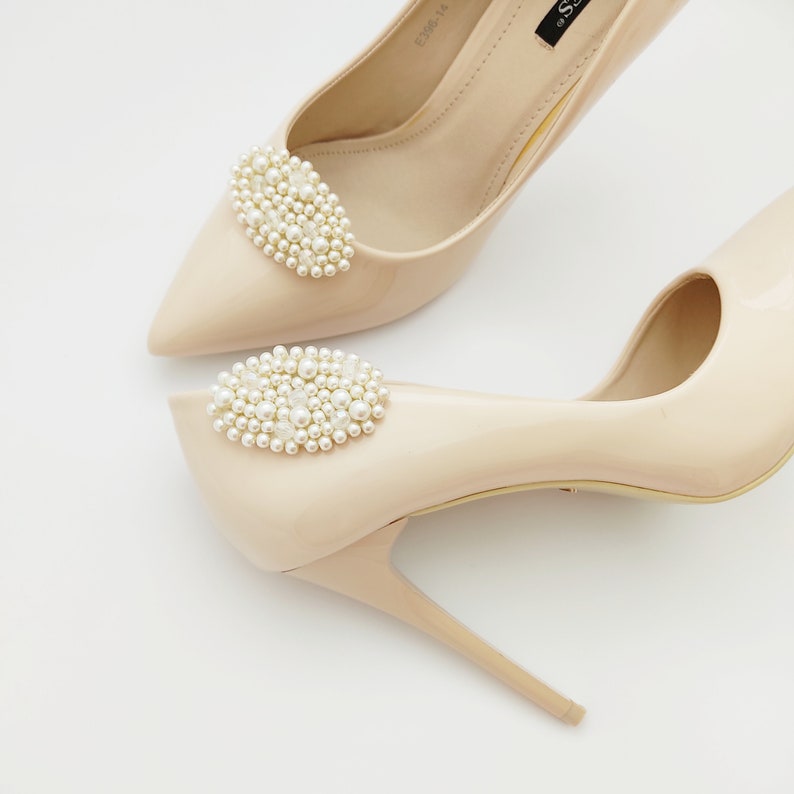 May include: A pair of nude high-heeled shoes with oval-shaped pearl embellishments on the toes.