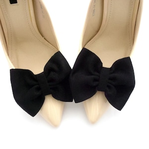 K&ouml;nnte beinhalten: Ein Paar beigefarbene High-Heel-Schuhe mit schwarzen Stoffschleifen an den Zehen.