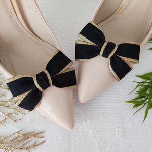 May include: A pair of nude pumps with black and gold ribbon bows on the toes.