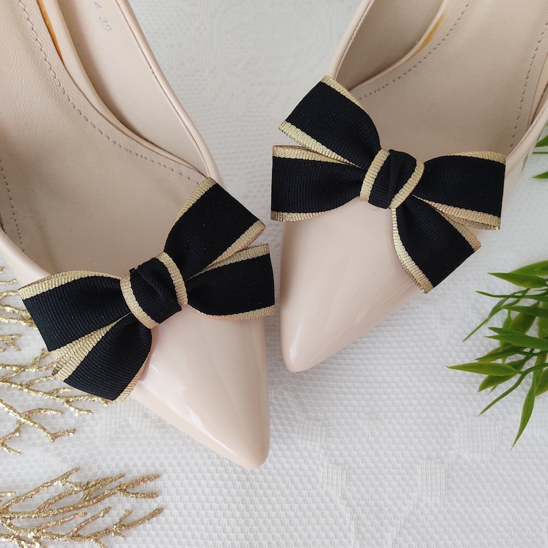 May include: A pair of nude pumps with black and gold ribbon bows on the toes.