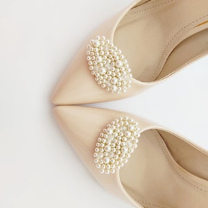 May include: A pair of beige pointed-toe shoes with pearl embellishments on the top of each shoe.