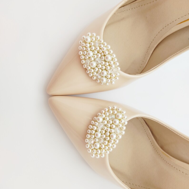 May include: A pair of beige pointed-toe shoes with pearl embellishments on the top of each shoe.