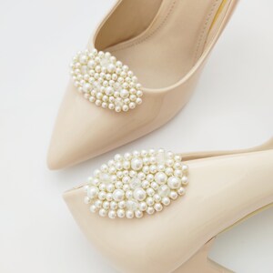 May include: A pair of beige high-heeled shoes with pearl embellishments. The shoes have a pointed toe and a delicate strap around the ankle.