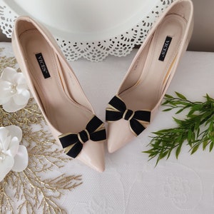 May include: A pair of nude-colored high heels with black bows. The heels have the word "VICES" written on the side.