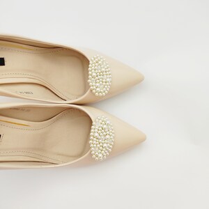 May include: A pair of beige pointed-toe pumps with a pearl embellishment on the toe.