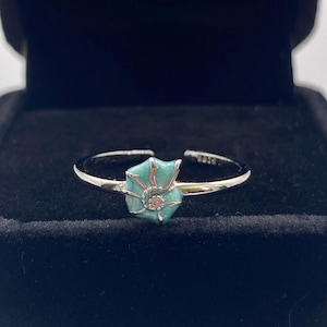 May include: A silver-toned open ring featuring a small, turquoise-coloured enamel seashell charm at the centre. The shell design includes delicate silver lines and a tiny, pale pink circular accent at its spiral core, set on a thin, polished band.