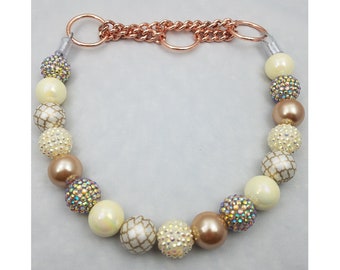 May include: A white and gold beaded necklace with a rose gold chain and clasp. The beads are various sizes and shapes, including round, square, and patterned.