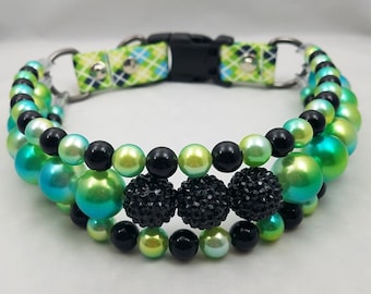 May include: A green, blue, and black beaded dog collar with a black buckle and two silver D-rings. The collar has three rows of beads, with larger black beads with rhinestones in the center.