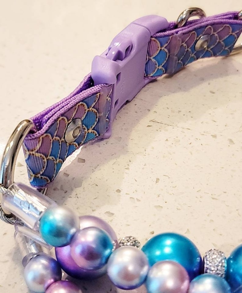 May include: A purple and blue patterned dog collar with a silver buckle and a matching beaded charm. The beads are iridescent and have a pearl-like finish.