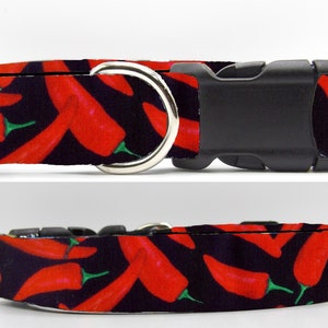 May include: A black dog collar with a red chilli pepper pattern. The collar has a black plastic buckle and a silver metal D-ring.