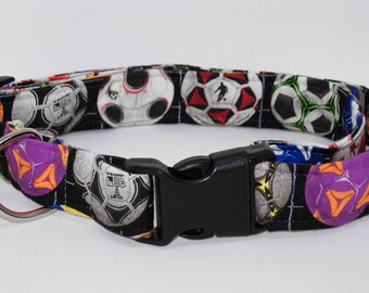 Può includere: Un collare nero per cani con un motivo ripetuto di palloni da calcio in vari colori. Il collare ha una fibbia in plastica nera e un anello a D in metallo argentato per l'attacco del guinzaglio. I palloni sono bianchi, rossi, verdi e viola.