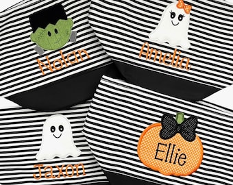 May include: Four Halloween-themed cosmetic bags with black and white stripes. Each bag features a different embroidered design: Frankenstein, a ghost, another ghost, and a pumpkin. Names are embroidered below each design: Nolan, Amelia, Jaxon, and Ellie.