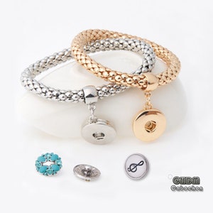 May include: Two silver and gold chain bracelets with snap charms. The charms are a silver circle with a turquoise rhinestone design, a silver circle with a plain design, a gold circle with a plain design, and a silver circle with a treble clef design.