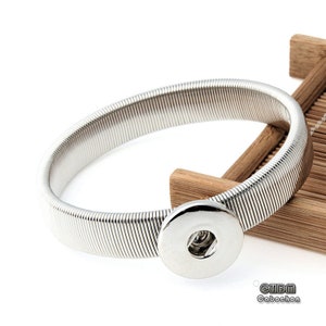 May include: A silver elastic bracelet with a snap closure. The bracelet is made of a stretchy metal and has a smooth, shiny finish.