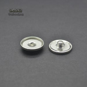 May include: Two silver-toned snap buttons, one with a flat top and the other with a raised dome top.
