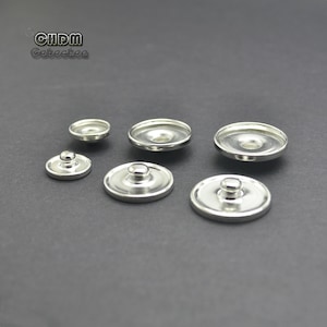 May include: Five silver-toned snap buttons of different sizes. The buttons are round and have a raised center.