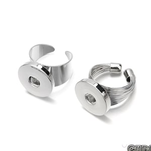 May include: Two silver-toned adjustable rings. One ring has a simple band, while the other features a twisted wire design. Both rings have a large, round, flat setting in the center, designed to hold a snap.