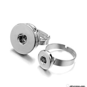 May include: Two silver rings with a round, flat, silver button on each. The button on the larger ring has a small hole in the center. The rings are for making jewelry.
