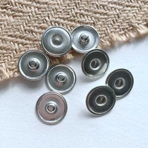 May include: A set of eight silver-toned snap buttons. The buttons are round and have a raised centre.