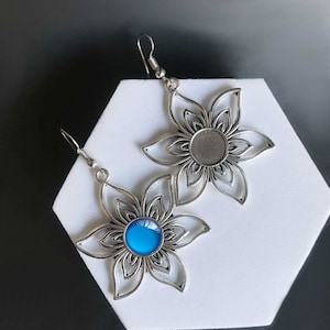 May include: A pair of silver flower-shaped earrings with a blue gemstone in one earring and a blank setting in the other.
