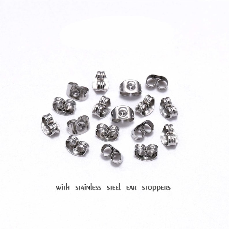 May include: A close-up of a group of silver earring backs, also known as ear stoppers, scattered on a white surface.  The text "with stainless steel ear stoppers" is printed below the earring backs.