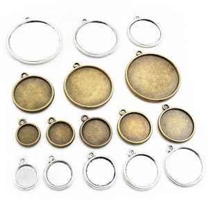 Op de afbeelding: Een verzameling ronde hangerbakjes in verschillende maten en afwerkingen. Sommige zijn zilverkleurig met een heldere glazen inzet, andere hebben een bronzen of antiek messing uitstraling. Elk bakje heeft een kleine lus om een ketting of koord aan te bevestigen.