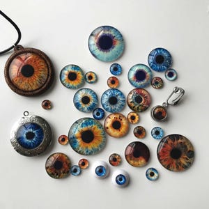 May include: A collection of eye-themed jewelry and craft supplies. Includes pendants, earrings, and glass cabochons with detailed iris designs in shades of blue, brown, and orange. Some pieces are set in metal or wood.
