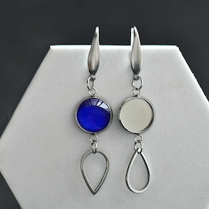 May include: A pair of silver dangle earrings with a teardrop-shaped pendant. One earring features a blue glass cabochon, while the other has a clear glass cabochon.