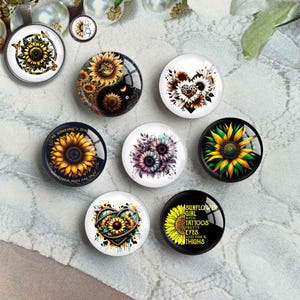 May include: Assortment of eight round glass cabochons with sunflower designs. The designs include a sunflower with a yin yang symbol, a sunflower heart, a sunflower with the text "Be someone's sunshine when their skies are gray", a sunflower with the text "Sunflower girl with tattoos pretty eyes and thick thighs", and a sunflower with a heart.