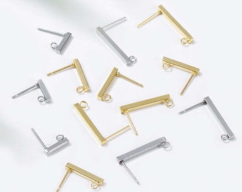 Può includere: Una collezione di basi per orecchini in oro e argento con forma a barra e un anello a salto. Le basi per orecchini sono sparse su una superficie bianca.