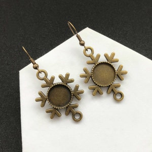 May include: A pair of bronze snowflake-shaped earring blanks with round, open-backed bezels. The bezels are approximately 1 inch in diameter.